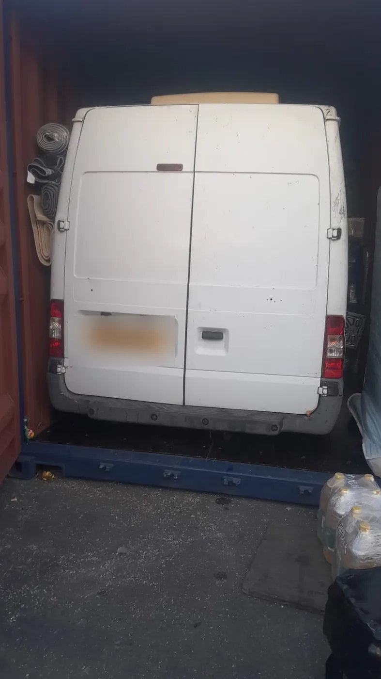 White van loaded inside a shipping container with cargo packed around it